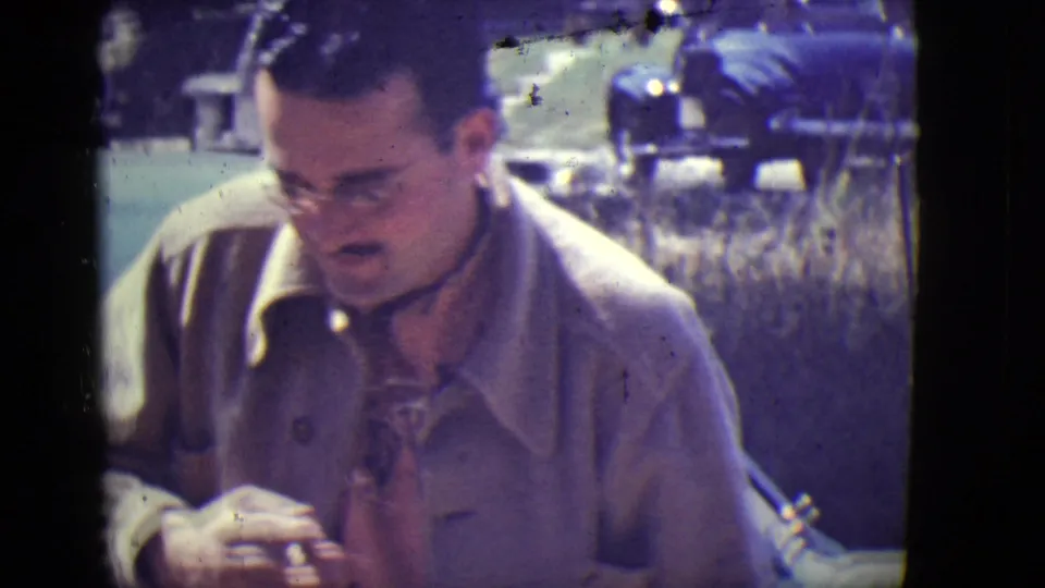 At the end of the East Orange clip, the man looks down beside the car, his glasses, coat, and patterned shirt still visible.