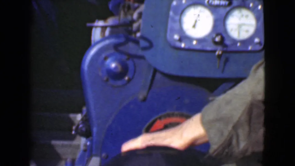 1946 Quebec 8mm frame showing a blue motorboat control panel, analog gauges, key, and a passenger's hand near the throttle area.
