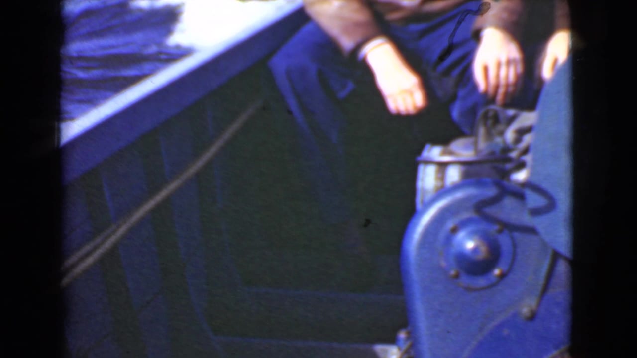 Partial view of a seated person beside a blue boat control housing and railing.