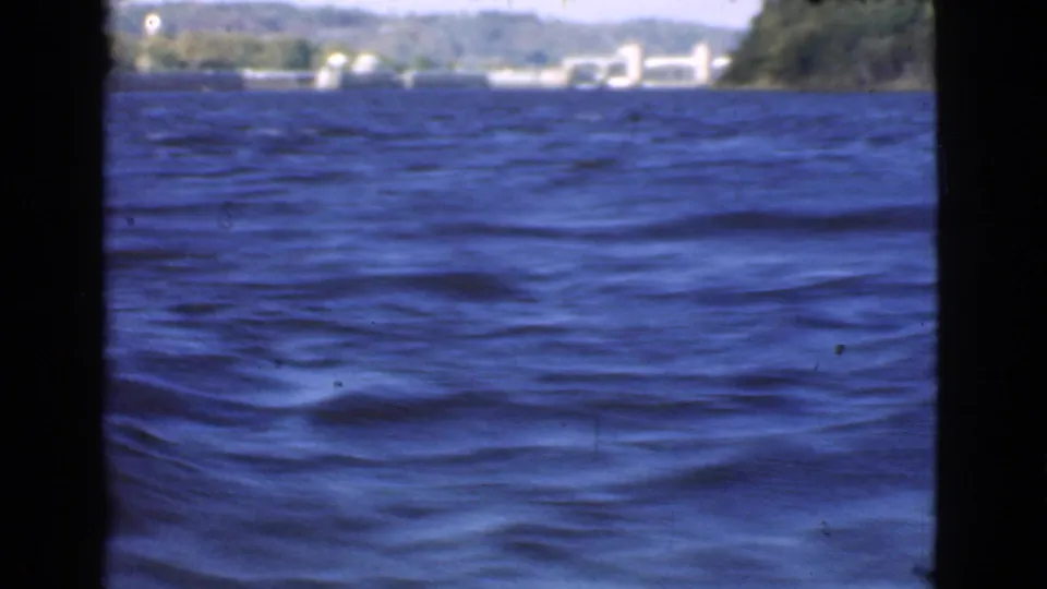 Open lake view in Quebec with rippling blue water, distant wooded shore, and small lakeside buildings visible.