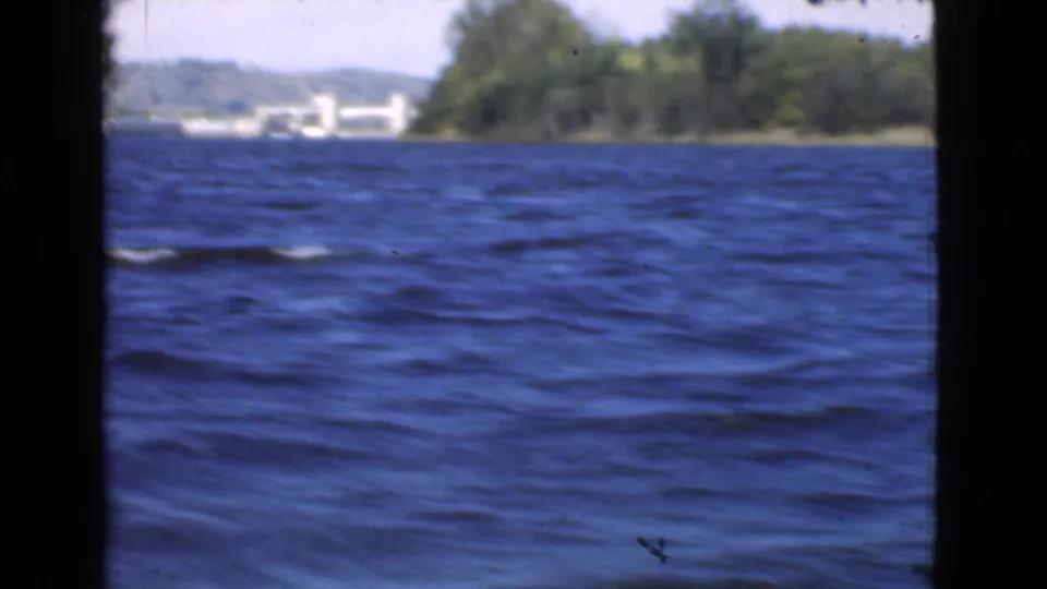 1946 Quebec 8mm frame showing blue water, distant trees, pale sky, and dark borders from a moving boat viewpoint.