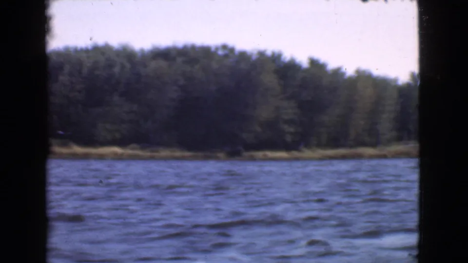 1946 Quebec home-movie still showing a green wooded bank beyond moving blue water.