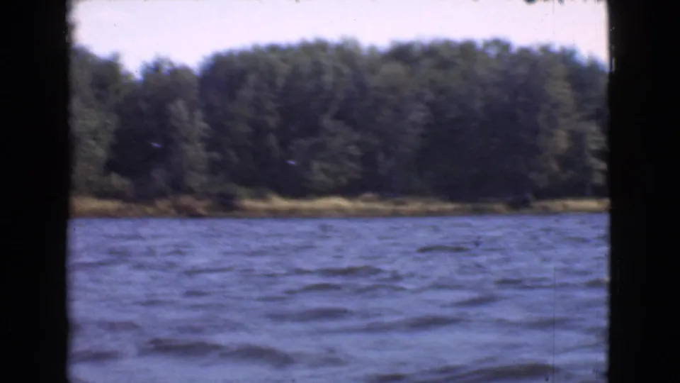 1946 Quebec 8mm view across rippling blue lake water toward a dense wooded shoreline, framed by dark gate edges.