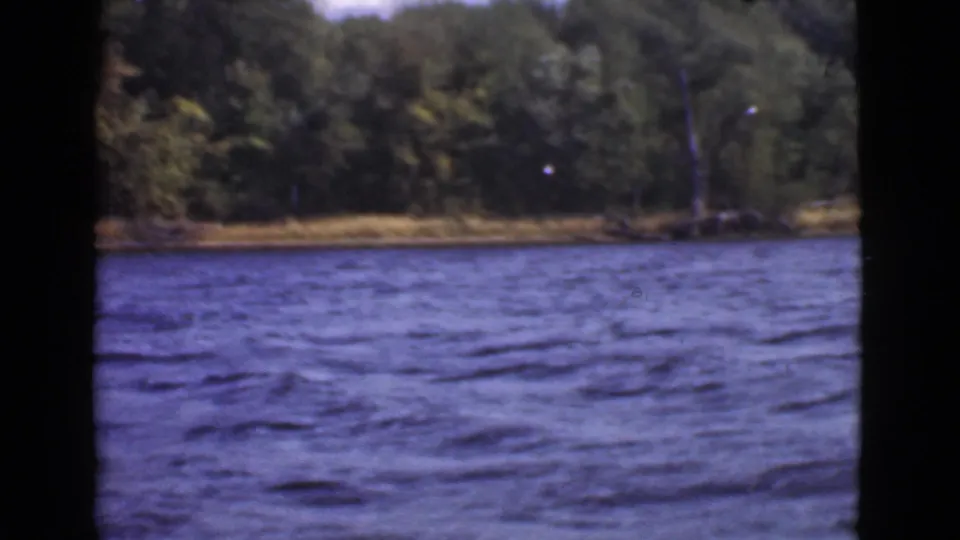 1946 Quebec home-movie frame showing blue lake water in the foreground and a dense green shoreline beyond.