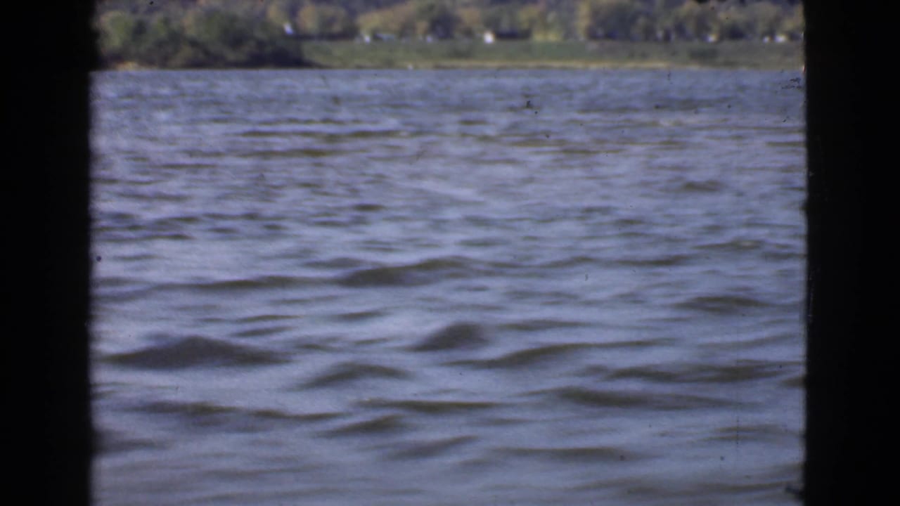 Rippling water seen past dark boat framing with a distant wooded shoreline.