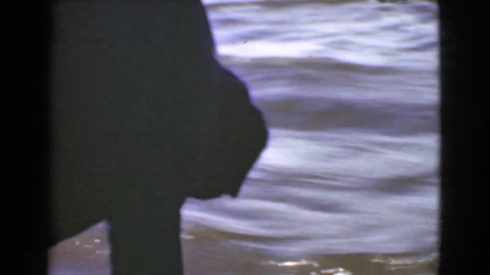 1946 Quebec 8mm frame with a dark dog silhouette partly obscured by boat structure beside bright, rippling water.
