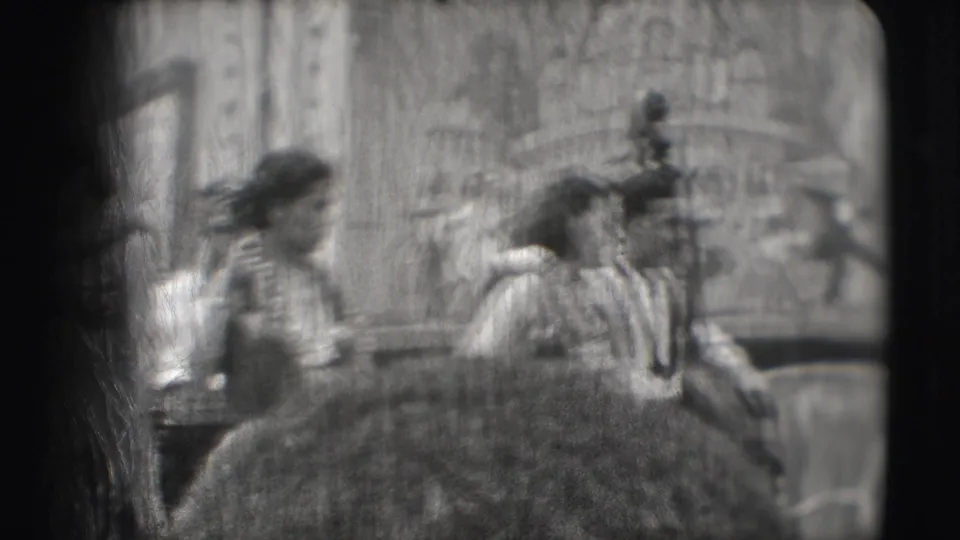 Soft, blurred 8mm frame of Ringling Brothers Sarasota performers moving past a large prop and tropical backdrop.