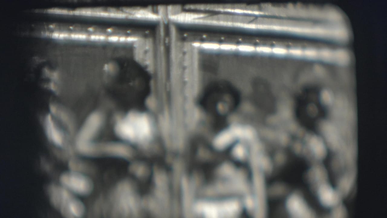 Soft black-and-white frame of three costumed women posing near a decorated backdrop.