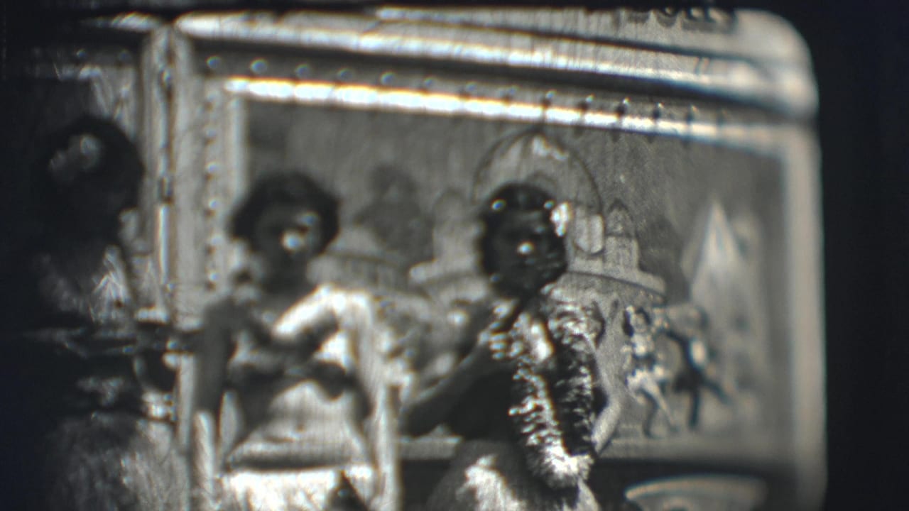 Two costumed women are clearer beside a decorated panel, with another figure partly visible.