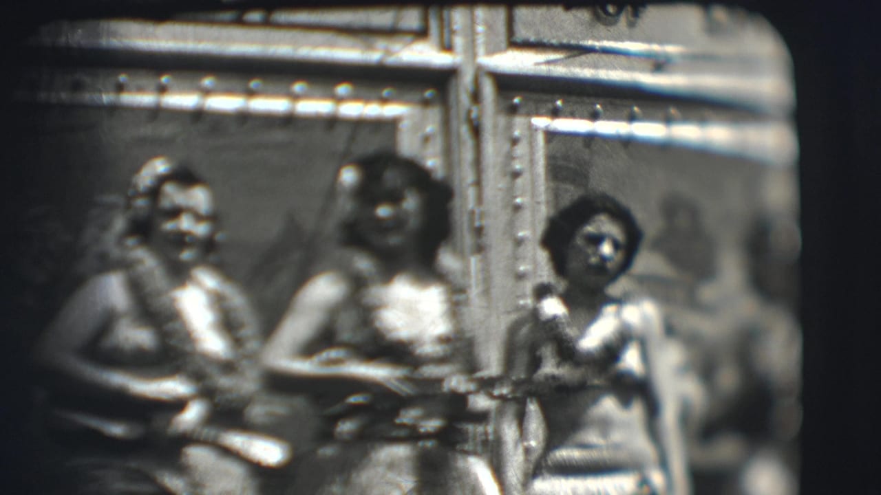 Three women wearing leis sit with small string instruments inside a tent.