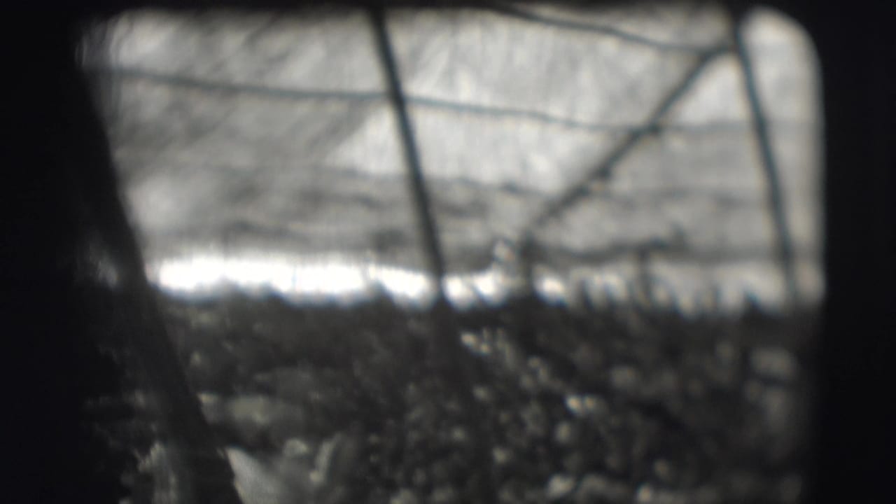 Obscured view through mesh toward a bright, crowded background with dark film borders.