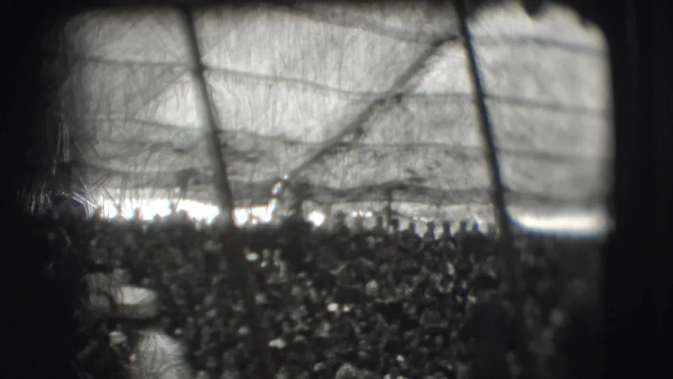 Metadata-supported 1948 Sarasota frame with an indistinct public gathering behind netting and strong light along the horizon.
