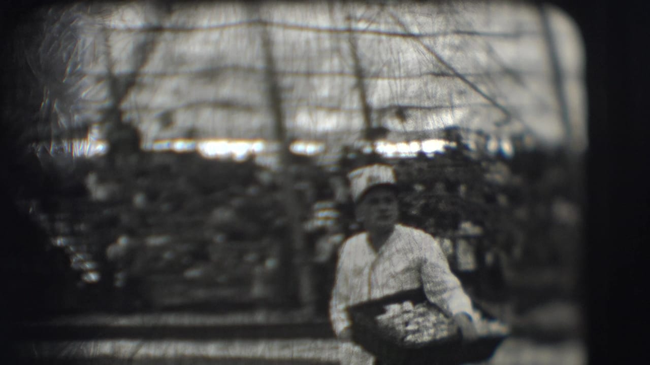 Uniformed man seated with a food tray in a large interior lined with cots.