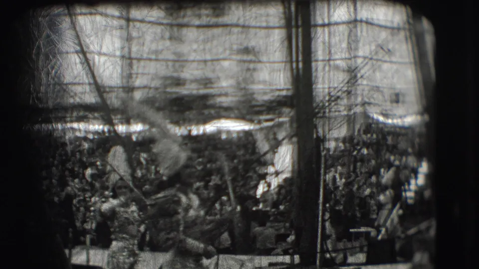 Black-and-white 8mm frame shows spectators, a flag or pole, and crowded parade activity within the Sarasota Ringling Brothers context supplied by metadata.