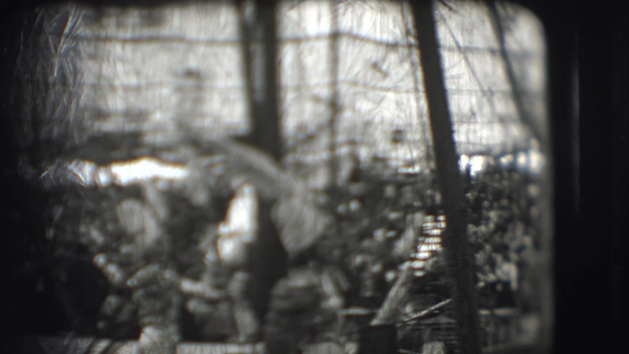 Costumed circus performers pass behind dark frame edges in a grainy black-and-white outdoor scene.