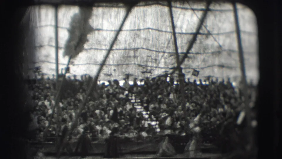 Packed Sarasota circus stands frame several indistinct figures near the arena, with scratches and exposure variation across the 8mm image.