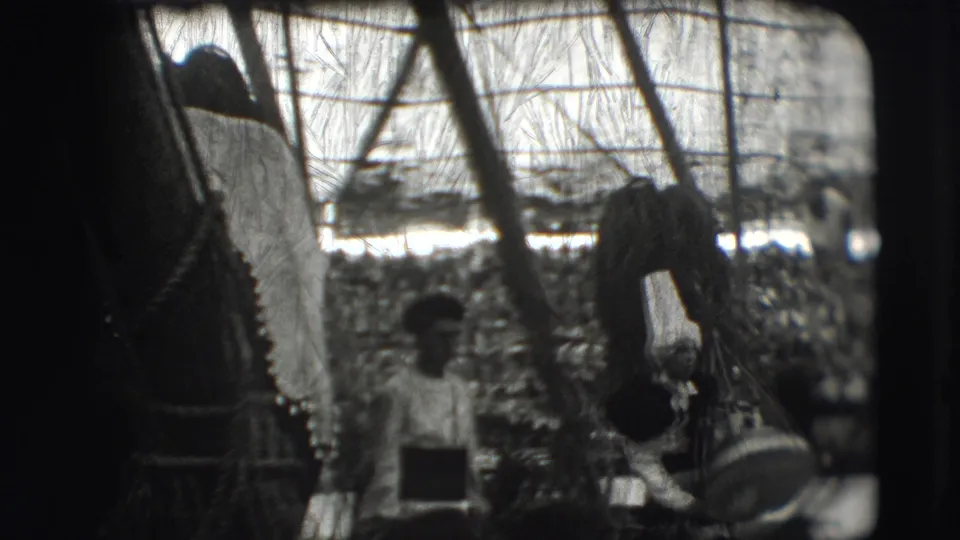 Inside the Sarasota circus tent, a costumed figure and another small figure appear near poles with the audience beyond.