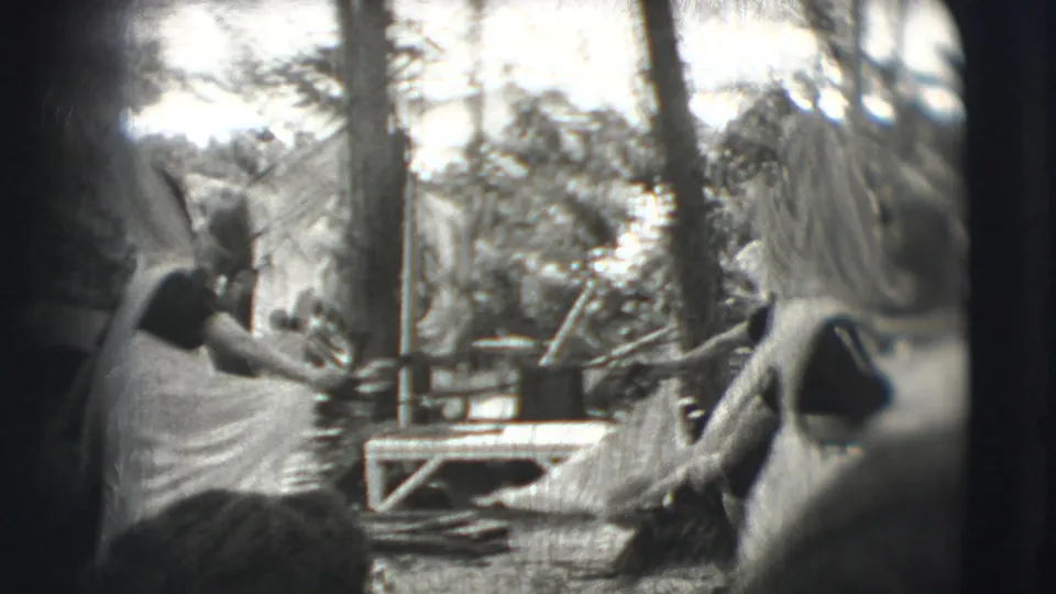 1948 Sarasota circus grounds footage showing a peacock near wooded enclosure rails while visitors stand partly in frame.