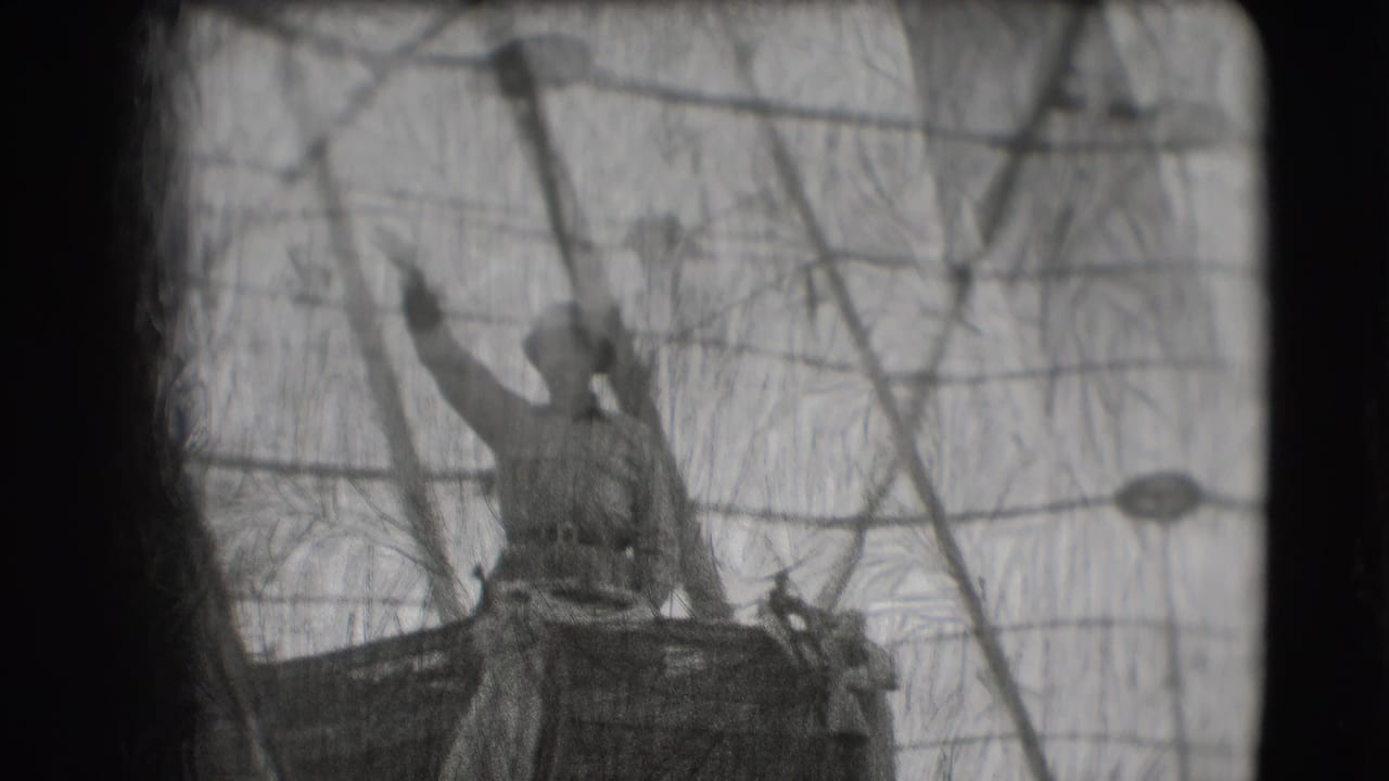 Uniformed man on a raised float waves behind a wire barrier during a parade.