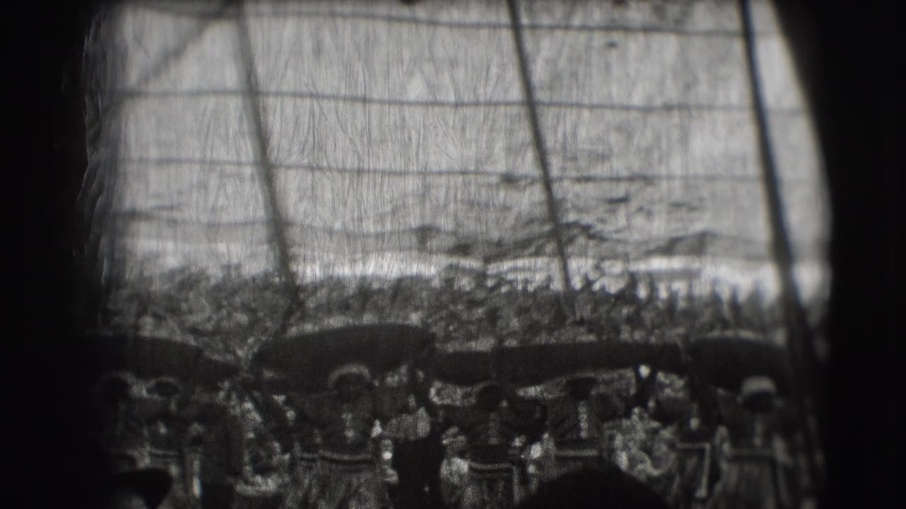 Crowd under a circus tent watching women carry broad objects on their heads.