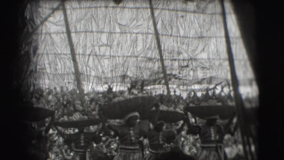 Black-and-white 8mm frame from the Sarasota circus performance, with women carrying broad objects on their heads before packed seating.