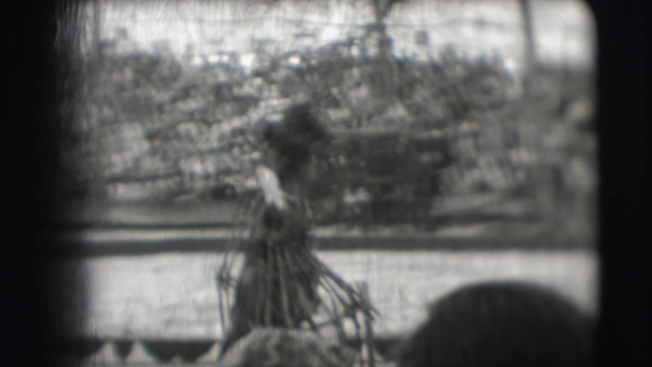 Costumed handler stands with a leashed bear near a wooden circus barrier.