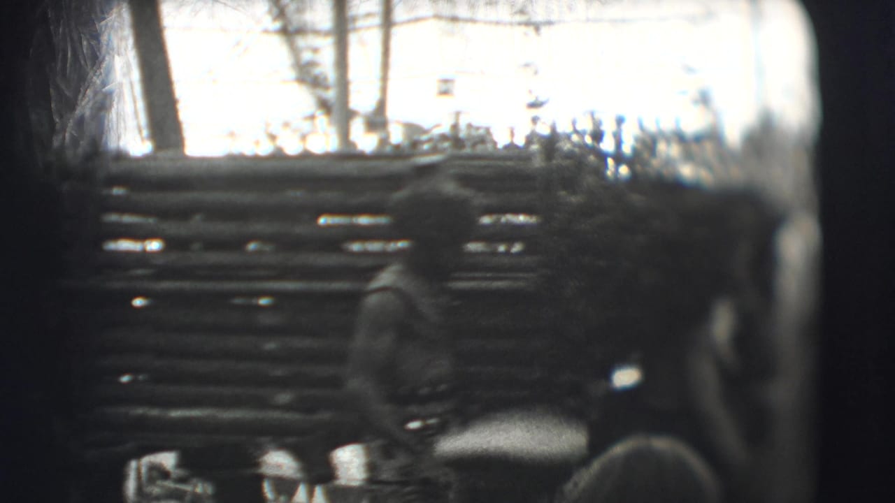 Spectators watch a figure moving past a log-style wooden enclosure.