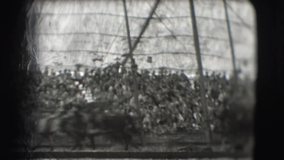 The frame shows the circus audience and tent supports in soft black-and-white focus, with the arena rail crossing the foreground.