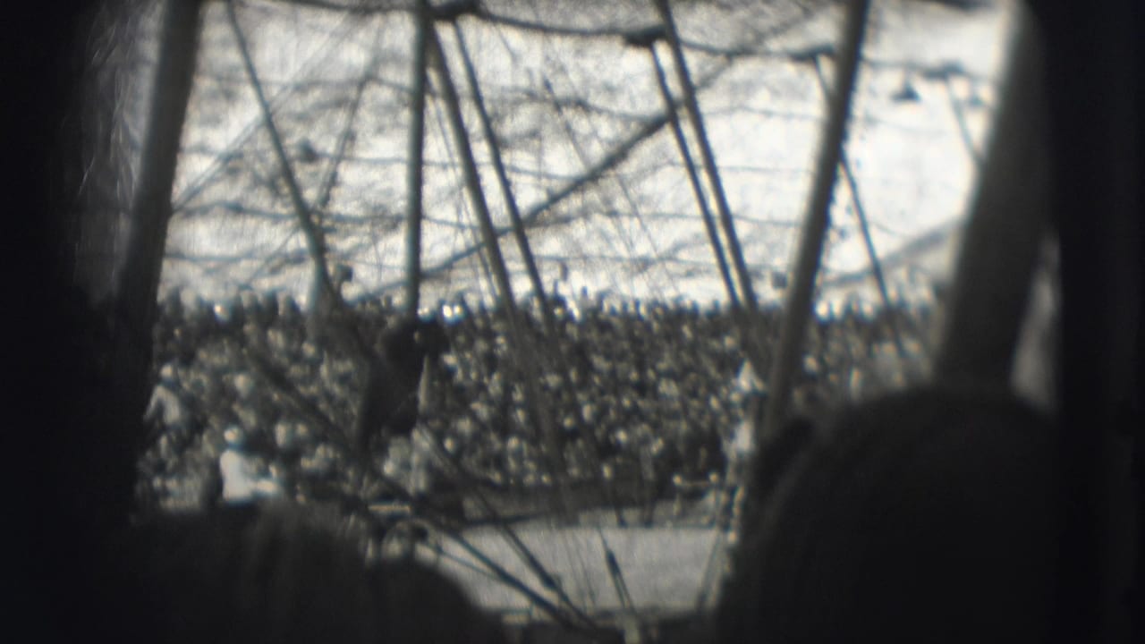 Blurred tent interior with poles, rigging lines, and audience across the ring.