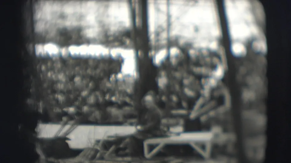A packed outdoor circus audience in Sarasota is visible beyond ring equipment and benches in soft black-and-white 8mm footage.
