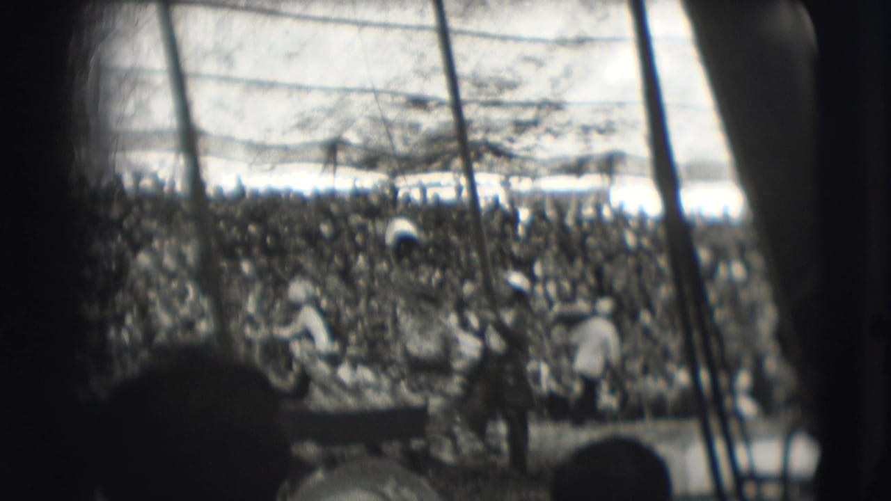 Black-and-white 8mm view of a circus arena with a large seated crowd and performers or handlers near the ring.