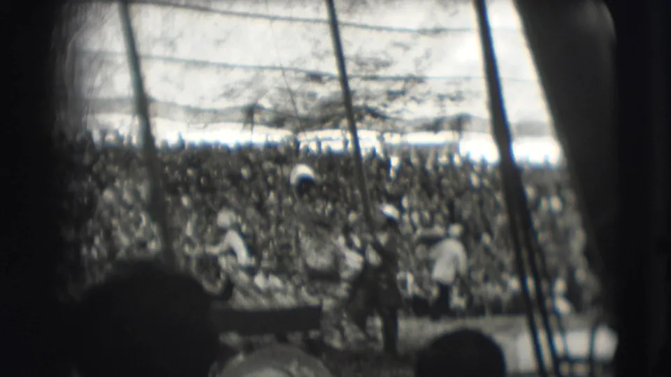 Black-and-white 8mm view of a circus arena with a large seated crowd and performers or handlers near the ring.