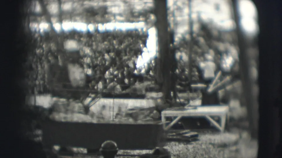 Spectator-shot Sarasota circus scene with crowded seating, ring equipment, and a bright figure or prop near the arena.