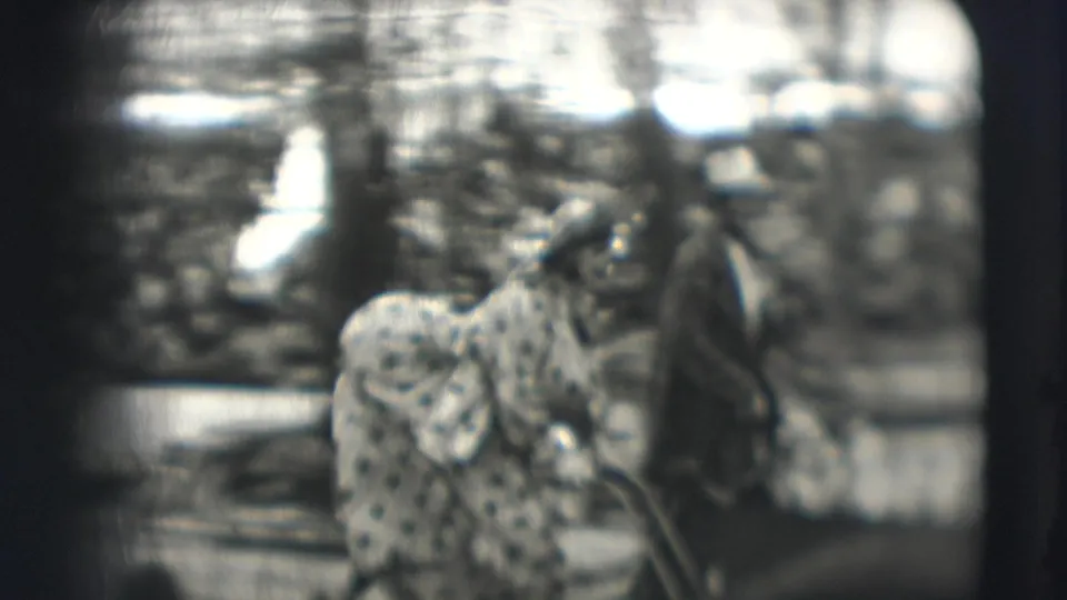 Black-and-white 8mm circus frame showing a spotted animal near the ring with a person nearby and audience behind.