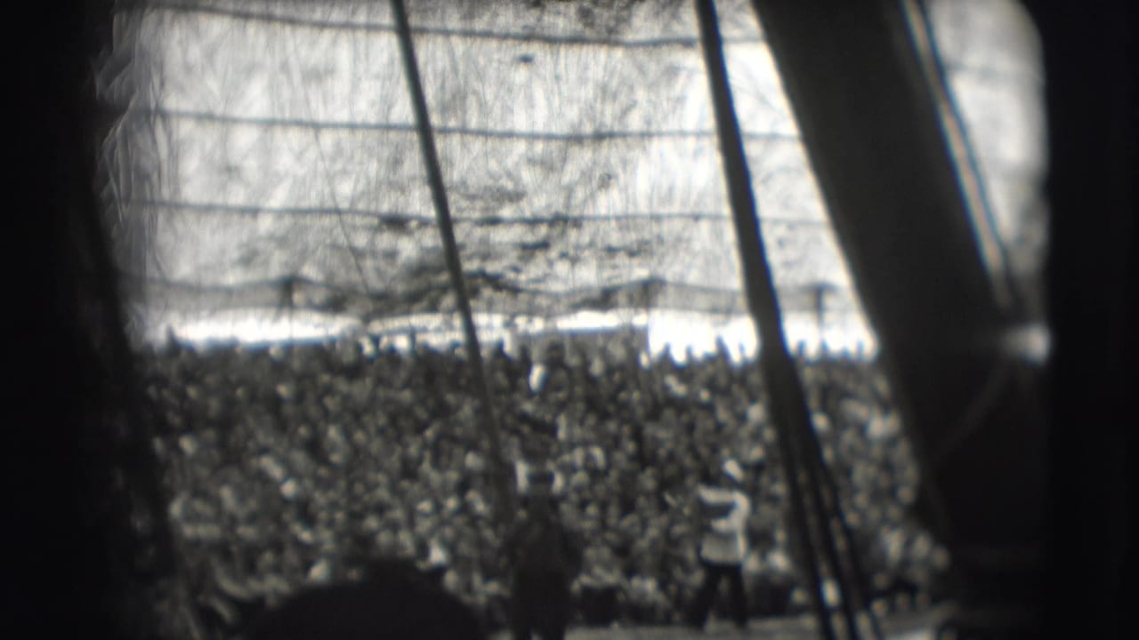 Crowded circus tent seen through dark poles and film gate edges.