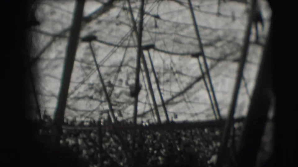 Grainy 1948 home-movie frame from Sarasota showing circus rigging and a small acrobat silhouette lower in the enclosure.