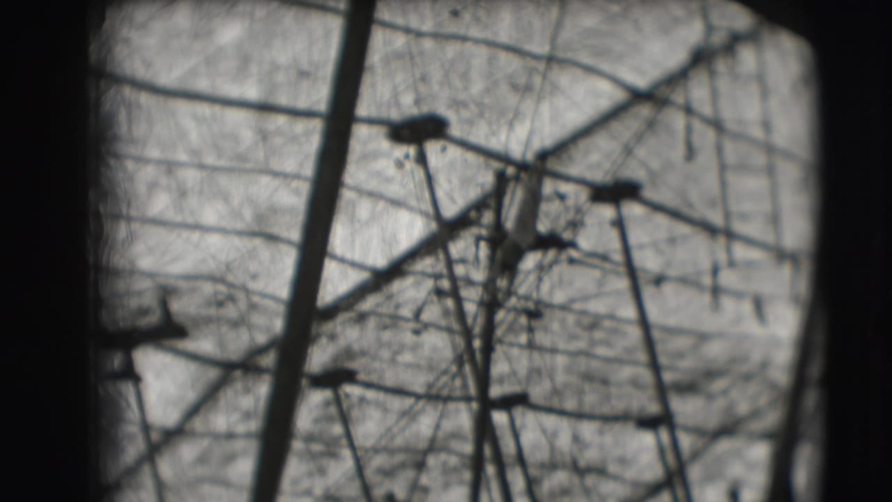Distant 1948 circus frame with high bar structure, support poles, netting, and a small acrobat form against the sky.