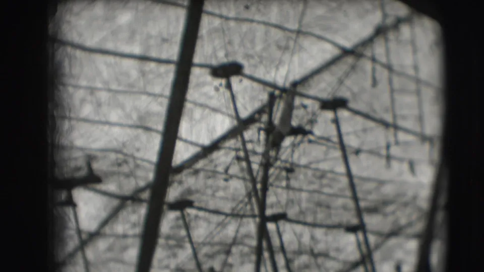 Distant 1948 circus frame with high bar structure, support poles, netting, and a small acrobat form against the sky.