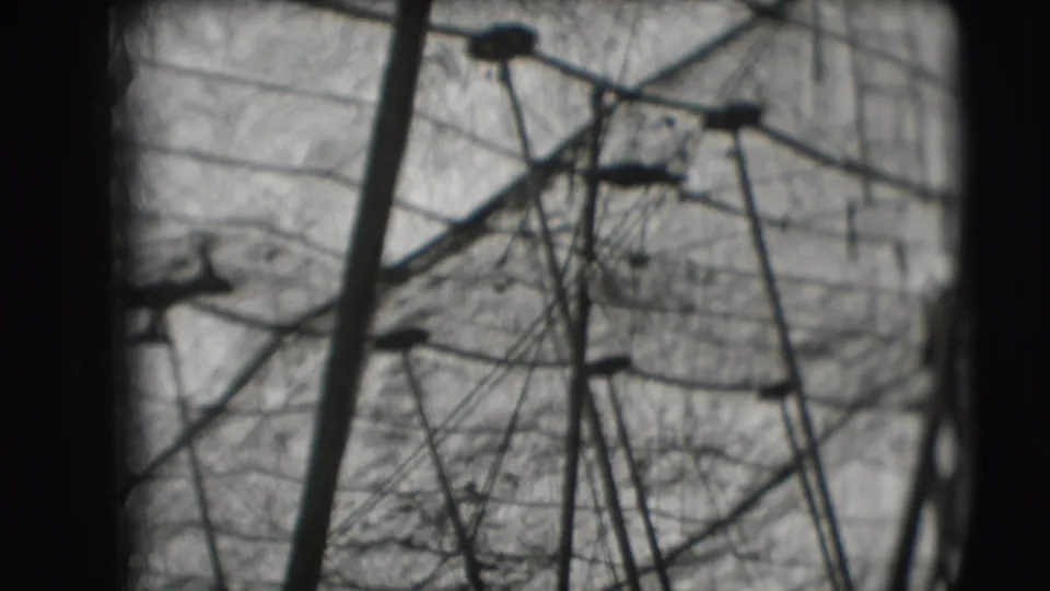 Soft black-and-white 8mm frame of the Sarasota circus high bar area with a distant acrobat, rigging, poles, and netting.