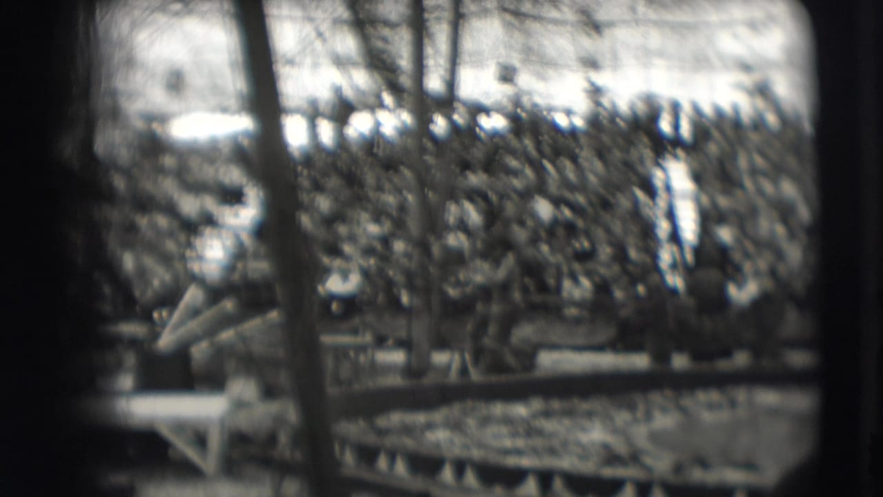 Crowded circus bleachers and rigging seen through a soft black-and-white 8mm frame.
