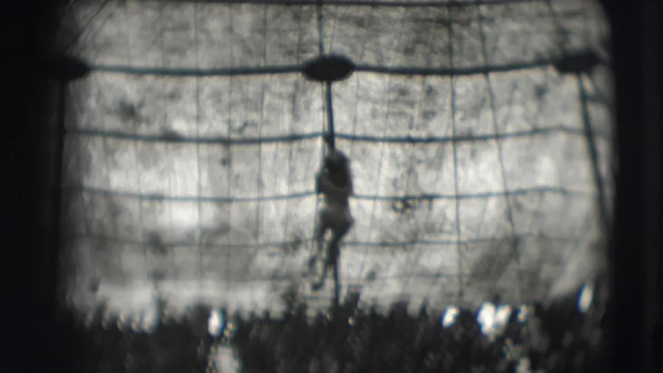 A high-wire performer appears silhouetted against the big-top canvas while climbing a central pole or rope in the ring area.