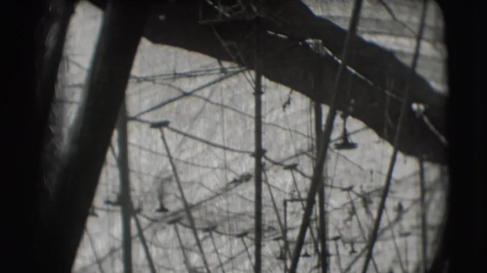 Vintage 8mm circus practice frame showing trapeze apparatus, vertical supports, and heavy dark framing from the camera position.