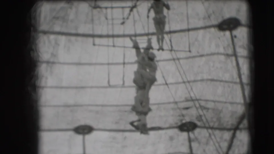 Low-angle 1948 circus view of trapeze artists hanging and balancing on high aerial equipment in Sarasota.