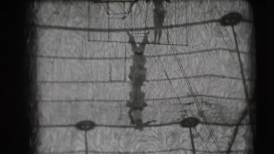 Final 1948 Sarasota frame with aerial performers on trapeze equipment, seen through scratched black-and-white 8mm film.