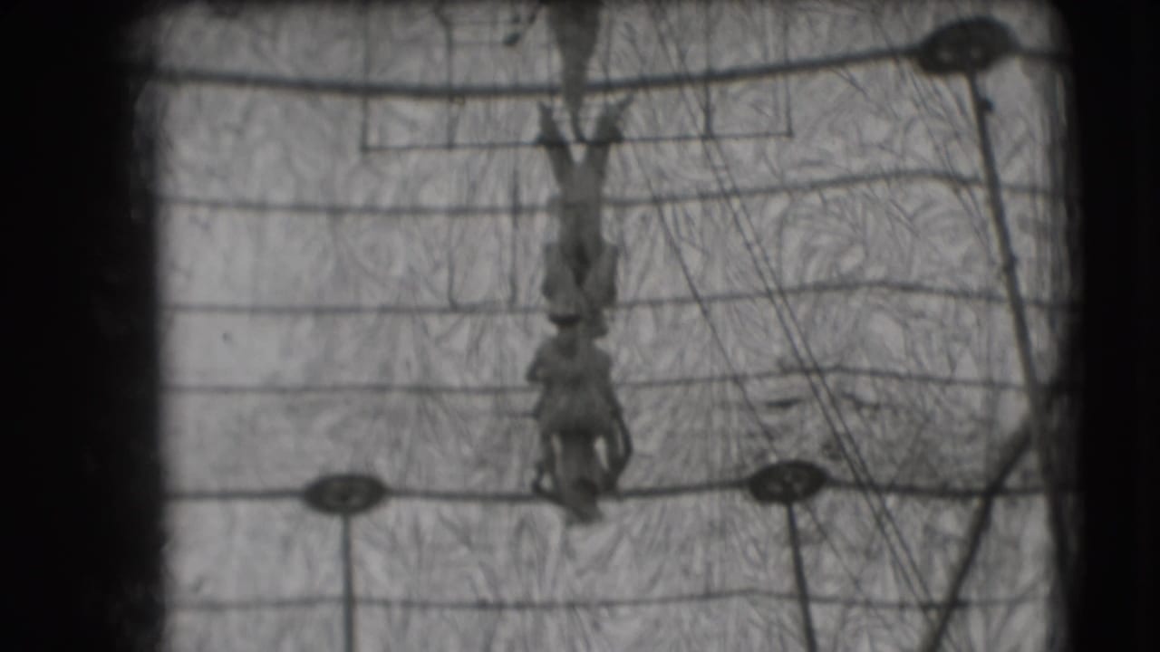 1948 Sarasota circus footage showing an inverted trapeze artist centered among overhead rigging, support cables, and poles.