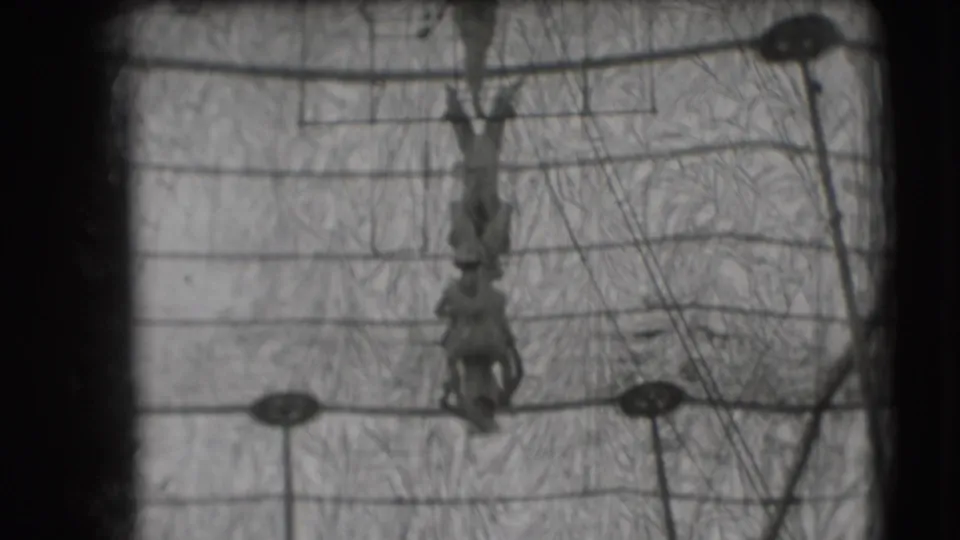 1948 Sarasota circus footage showing an inverted trapeze artist centered among overhead rigging, support cables, and poles.