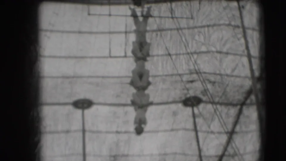 1948 Ringling Brothers Sarasota home-movie frame showing a trapeze performer below the bar with circus rigging and cables behind.