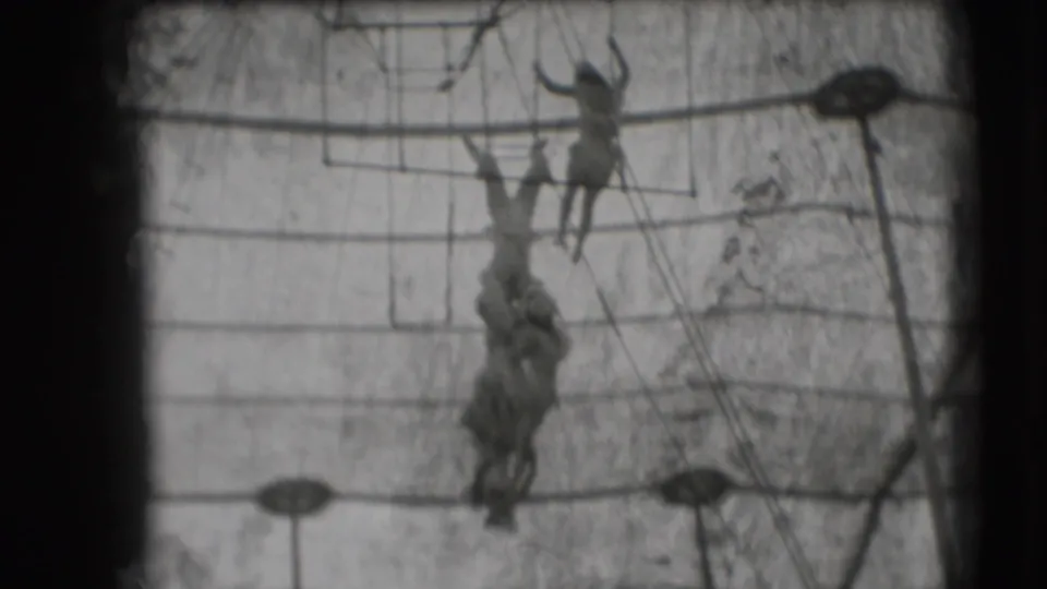 In 1948 Sarasota circus footage, two women trapeze performers hang at different heights within ropes and overhead bars.