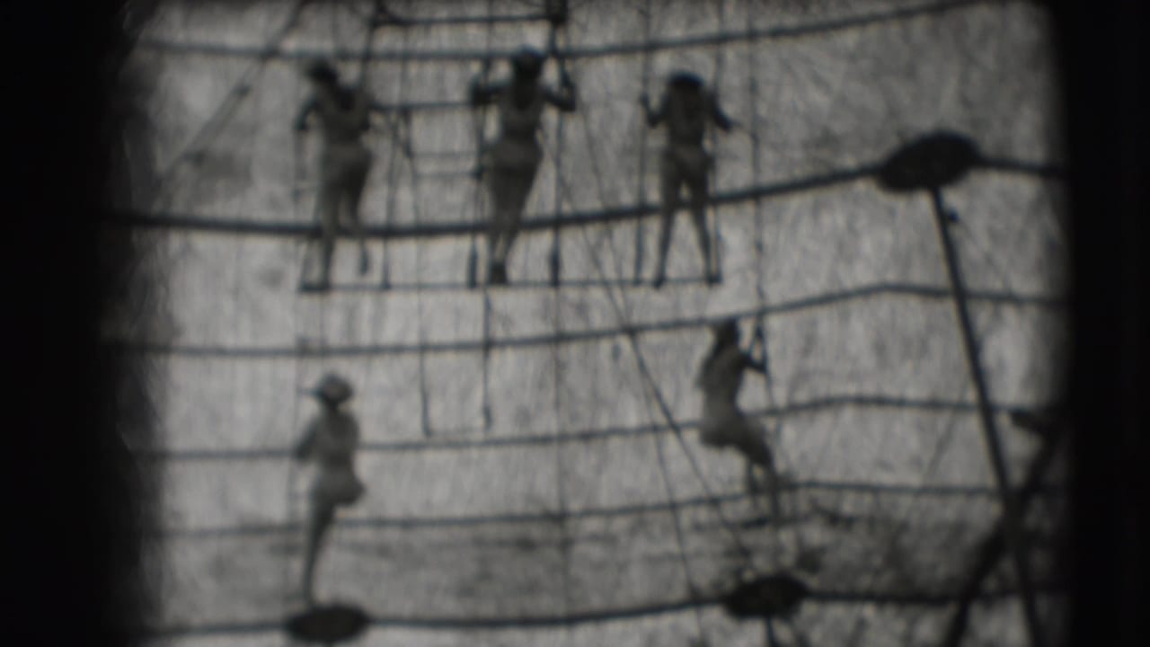Small figures in light clothing climb across rope rigging in a soft black-and-white frame.