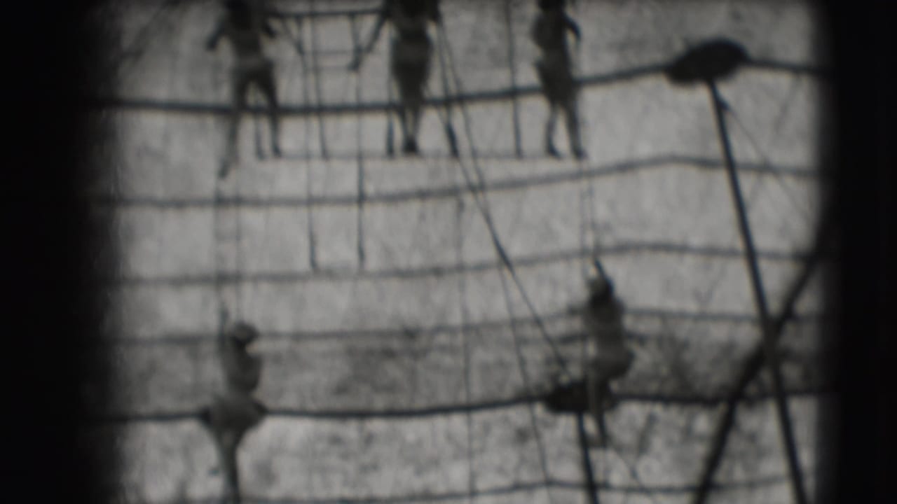 Distant climbers move among horizontal and vertical ropes with dark film borders.